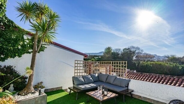 A patio with a sofa, a small table, and a palm tree. - La Terraza de Ribadesella - country house in Ribadesella, Northern Spain (Ribadesella)