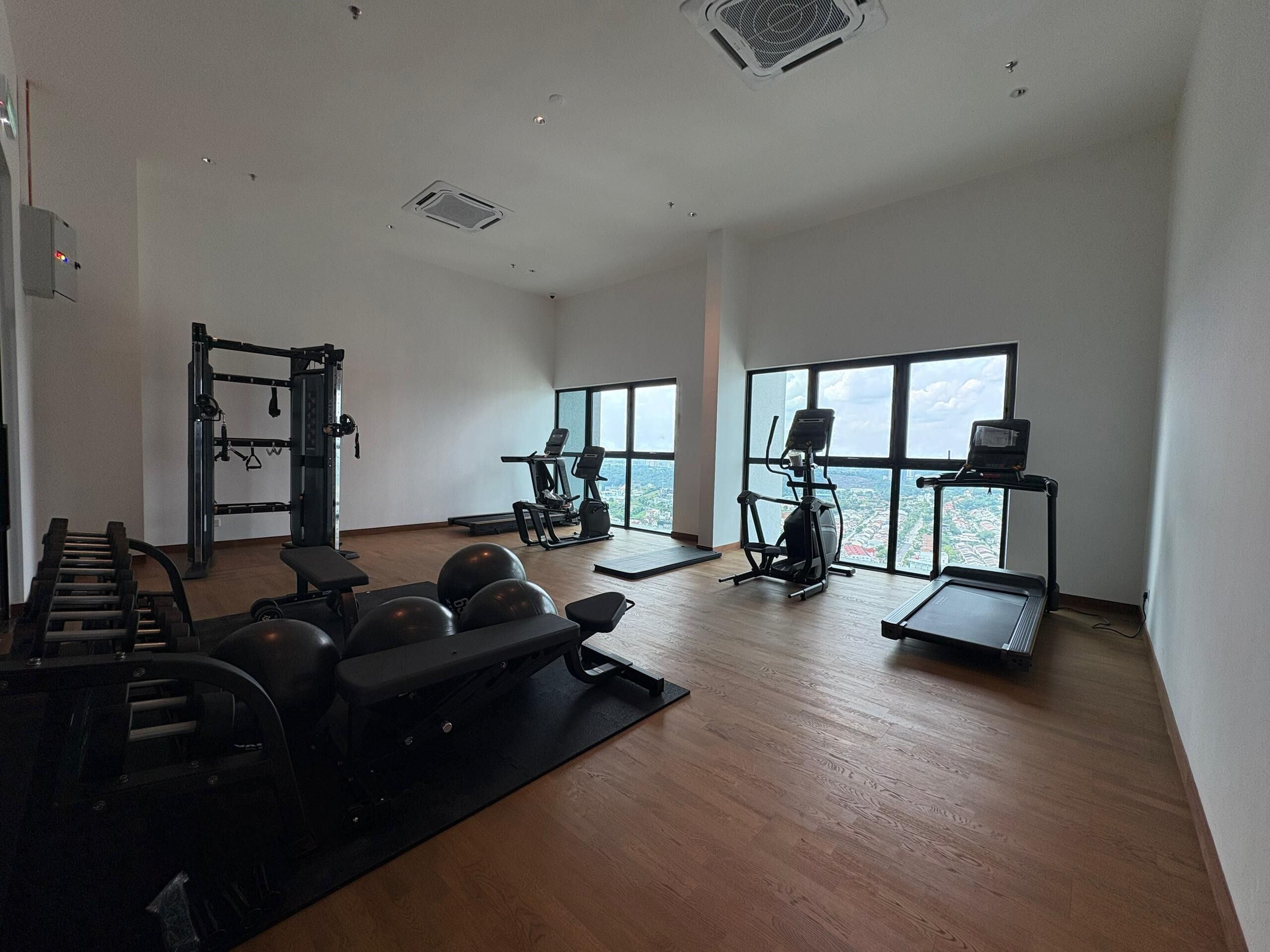 A spacious gym with various exercise equipment, large windows offering a city view, and a clean, modern interior.