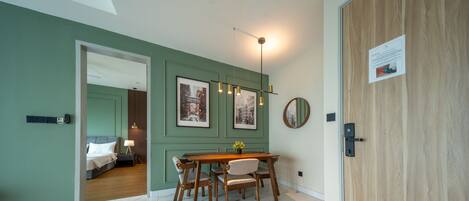 A dining area with a wooden table and chairs, framed pictures on the wall, and a ceiling light fixture.