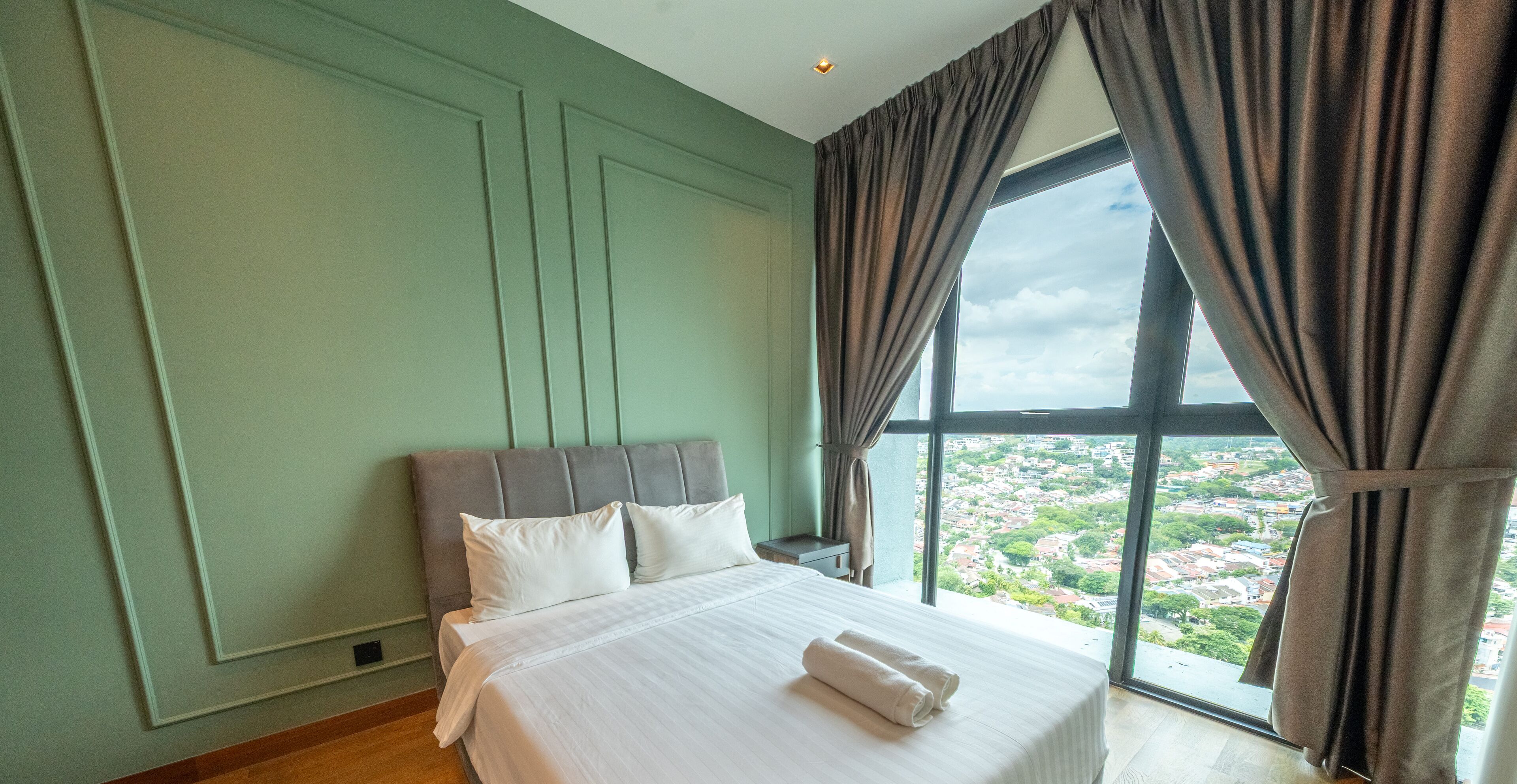 Ein Schlafzimmer mit einem großen Bett, Blick auf eine Stadtlandschaft durch ein Fenster und grünen Wänden.