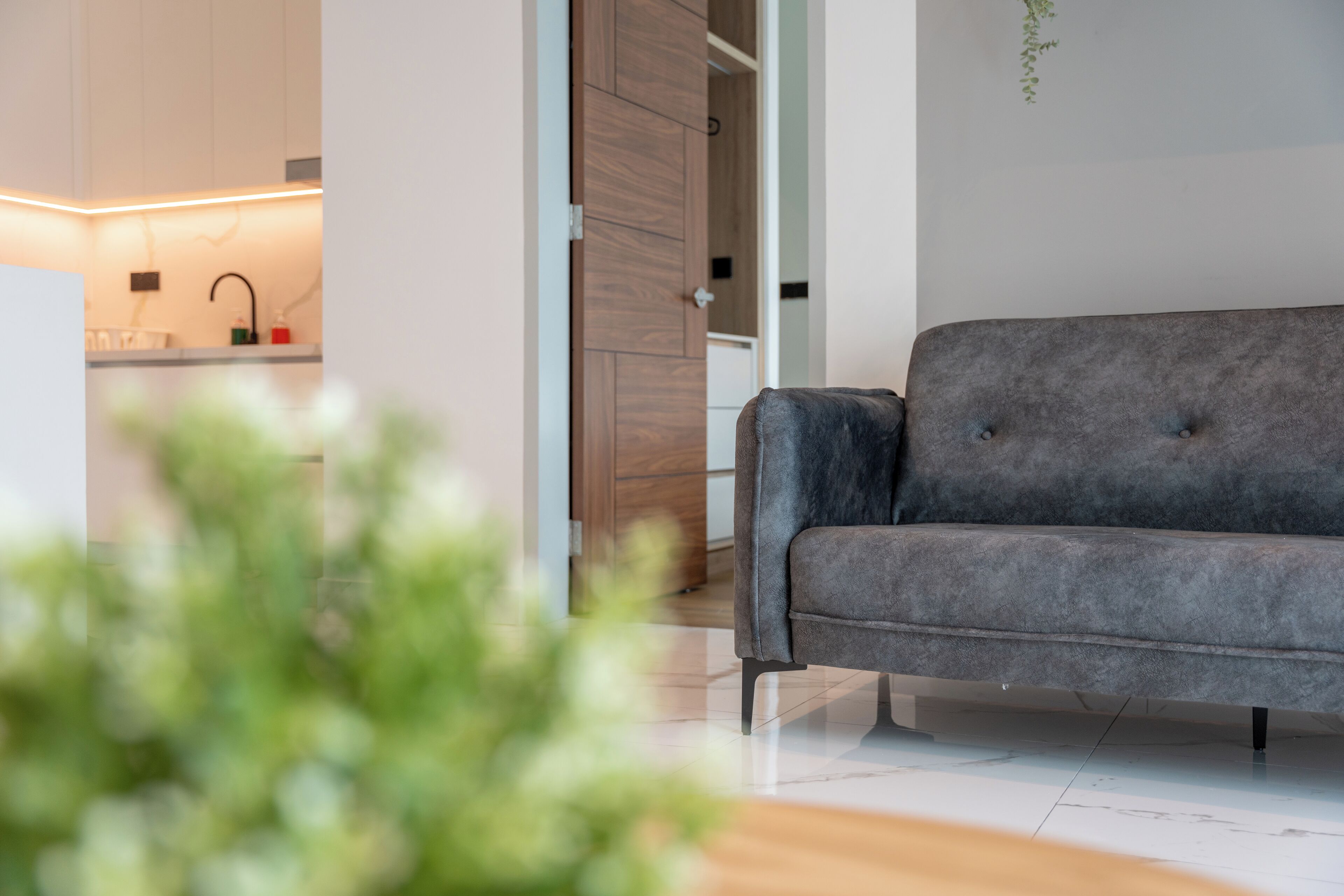 A modern living room with a grey sofa, a wooden cabinet, and a white tiled floor.
