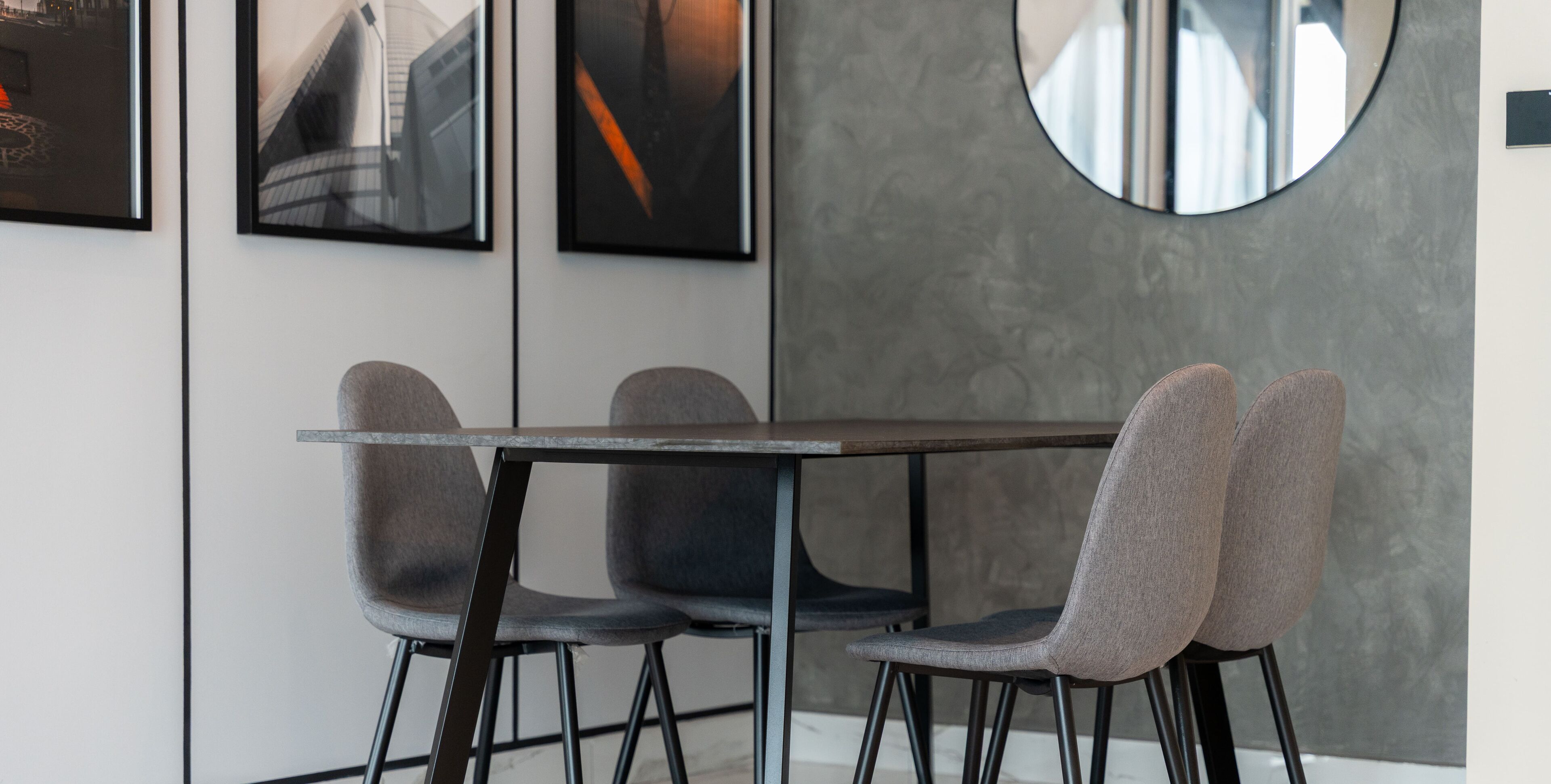 A modern dining area with a rectangular table and four grey upholstered chairs.