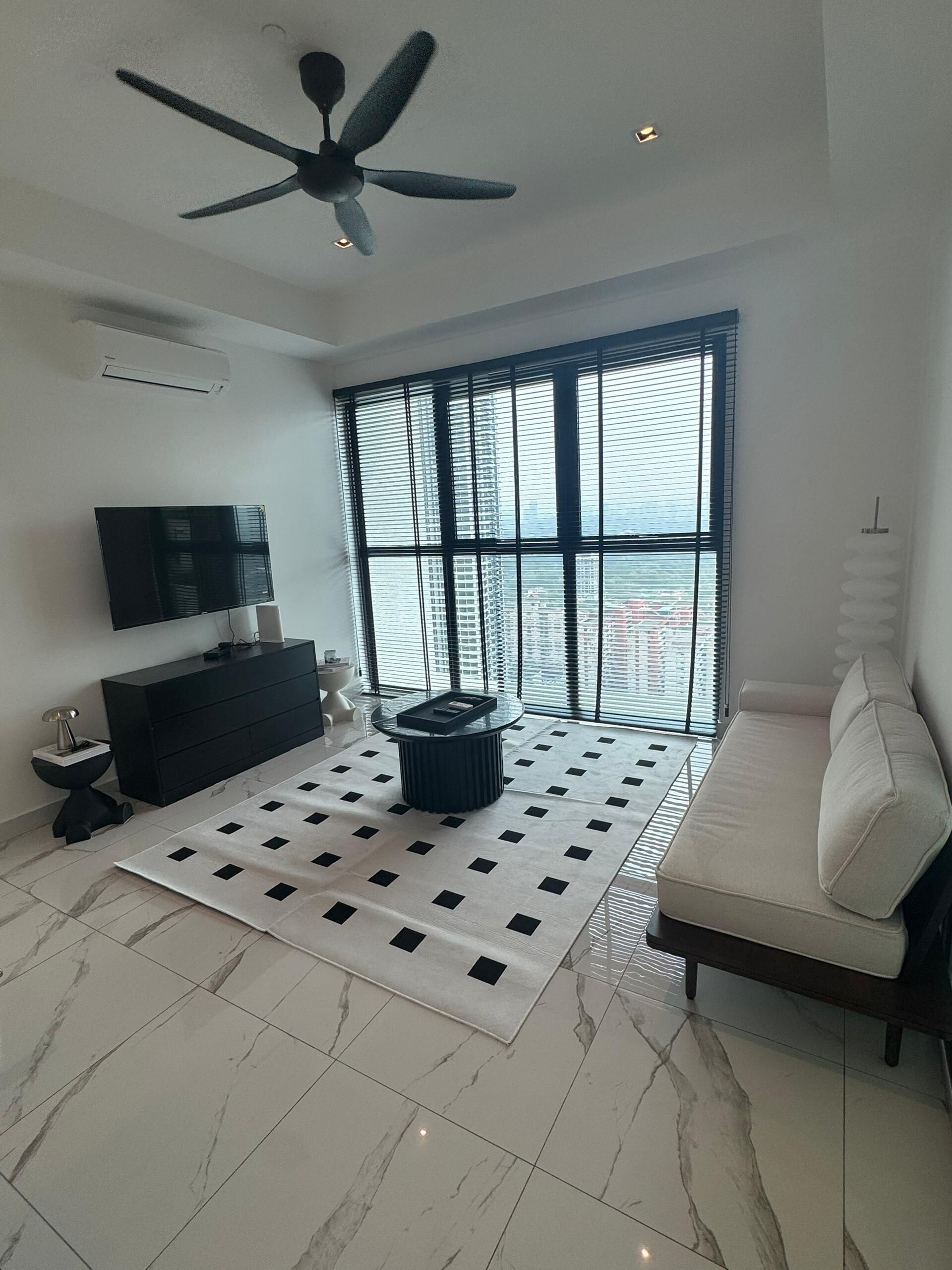 A modern living room with a ceiling fan, a black TV on the wall, a black sofa, a white sofa, a black coffee table, and a patterned rug.
