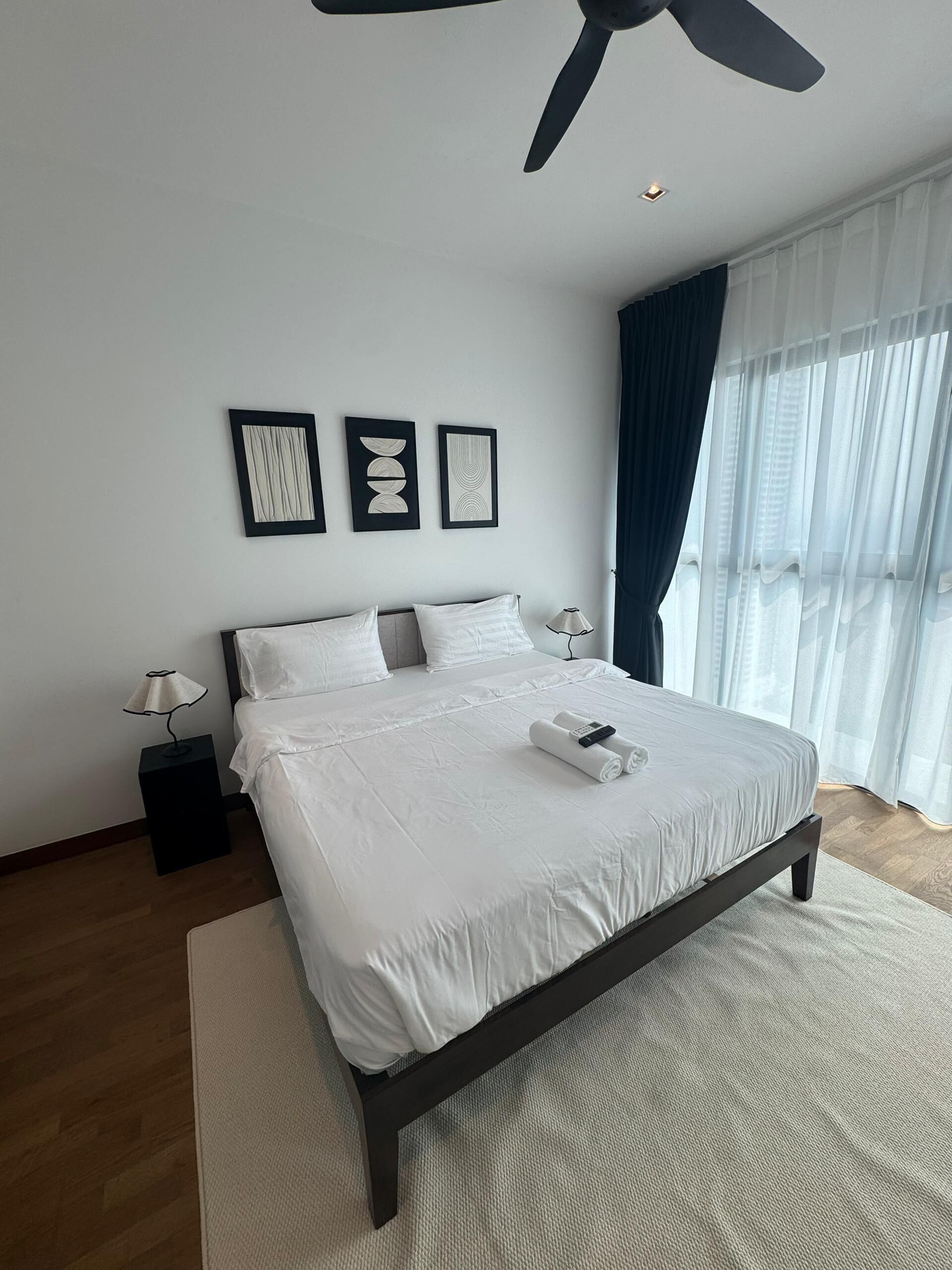 Ein modernes Schlafzimmer mit einem großen Bett, einem Deckenventilator und Blick ins Freie durch transparente Vorhänge.