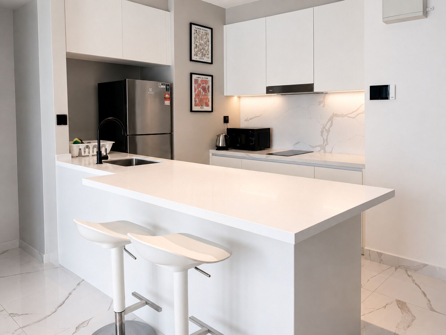 Eine moderne Küche mit einer großen Kochinsel, weißen Barhocker, Edelstahlgeräten und einer Marmor-Spritzschutzwand.