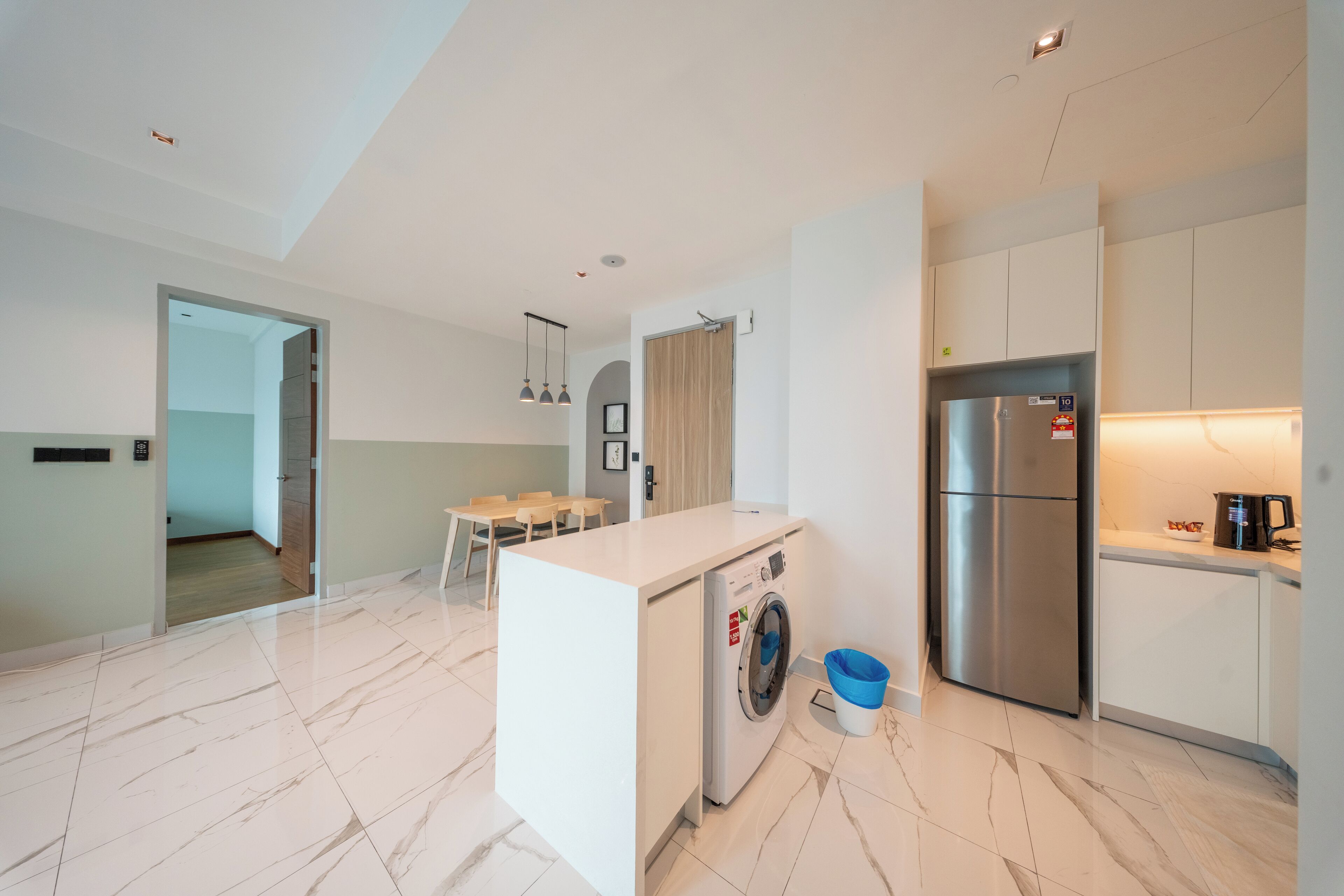 A modern kitchen with a built-in washing machine, a stainless steel refrigerator, and a dining area with a table and chairs.