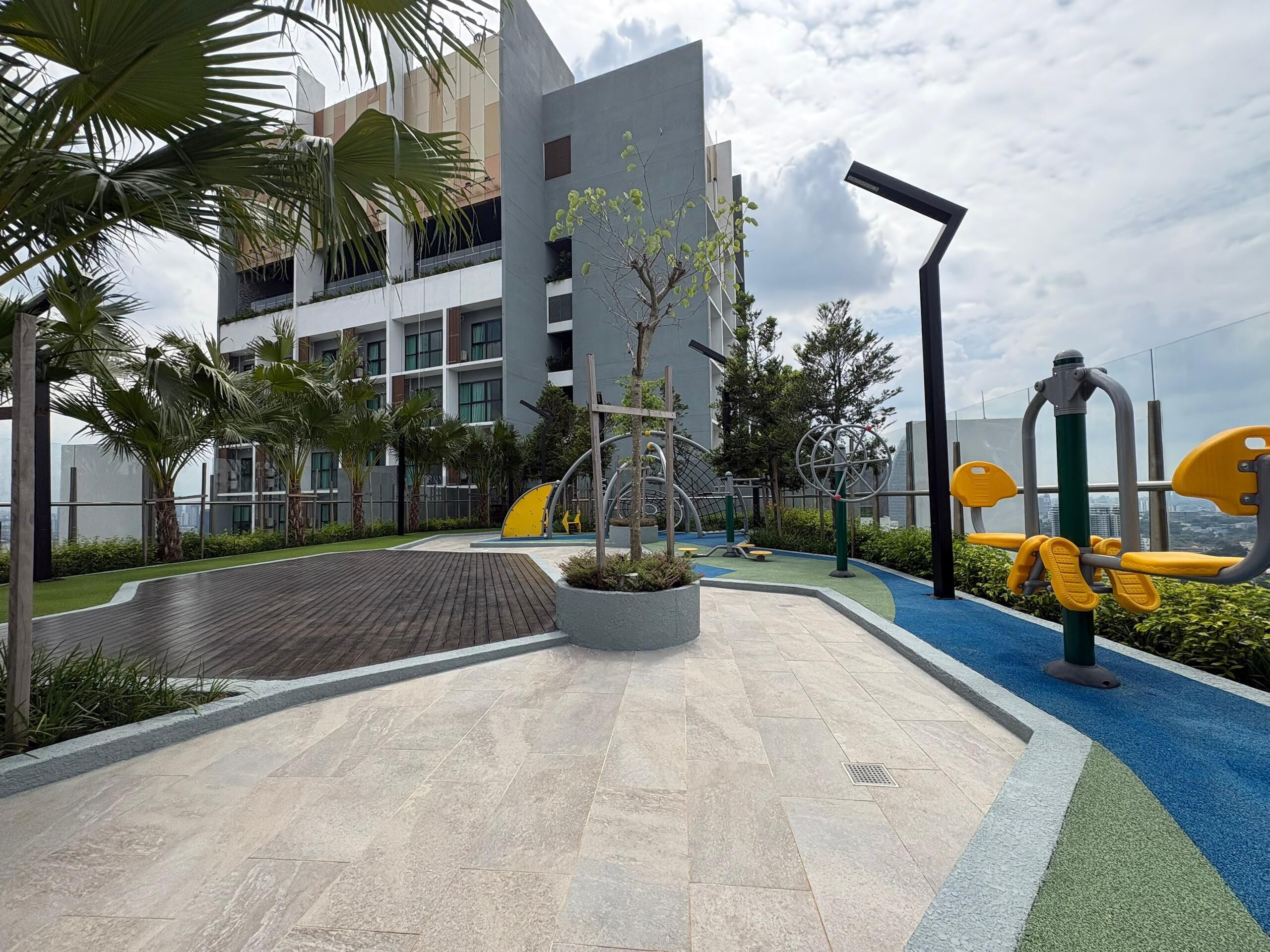 Un espacio exterior moderno con equipamiento de ejercicio, un sendero pavimentado y un edificio con balcones.