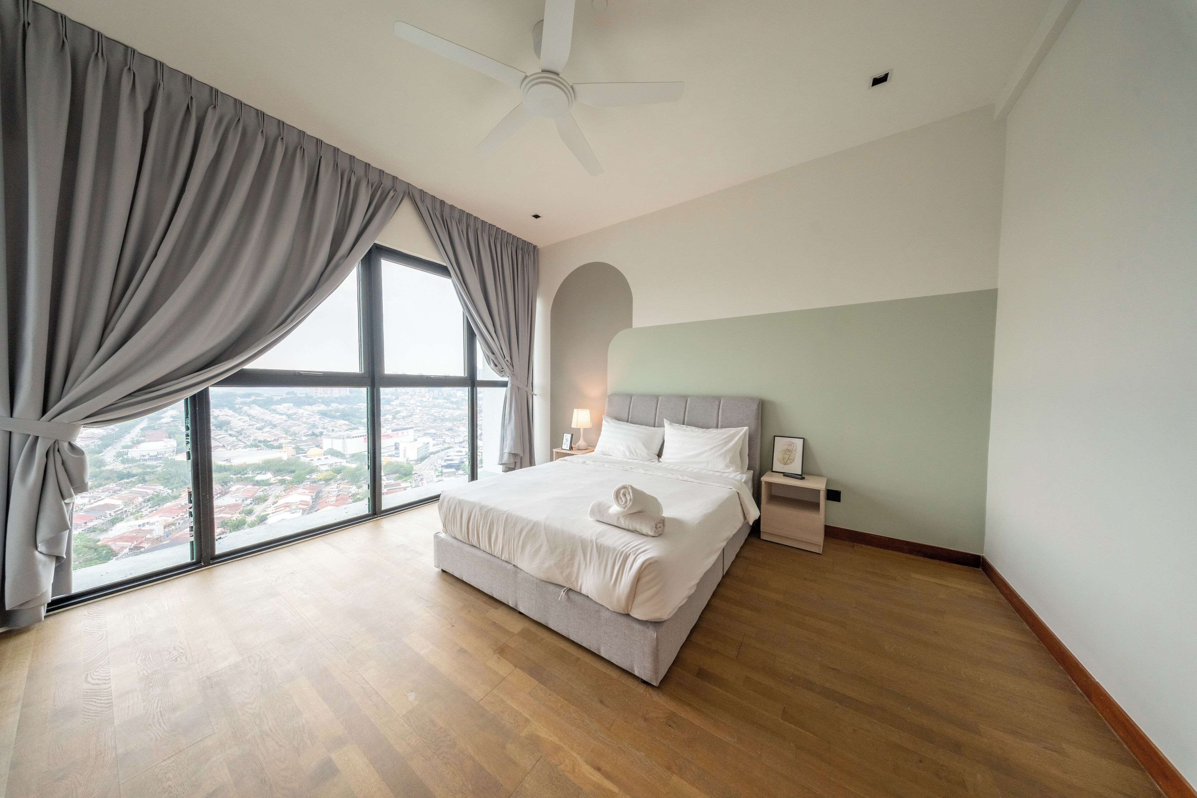 A bedroom with a large window, a bed, a ceiling fan, and a nightstand.
