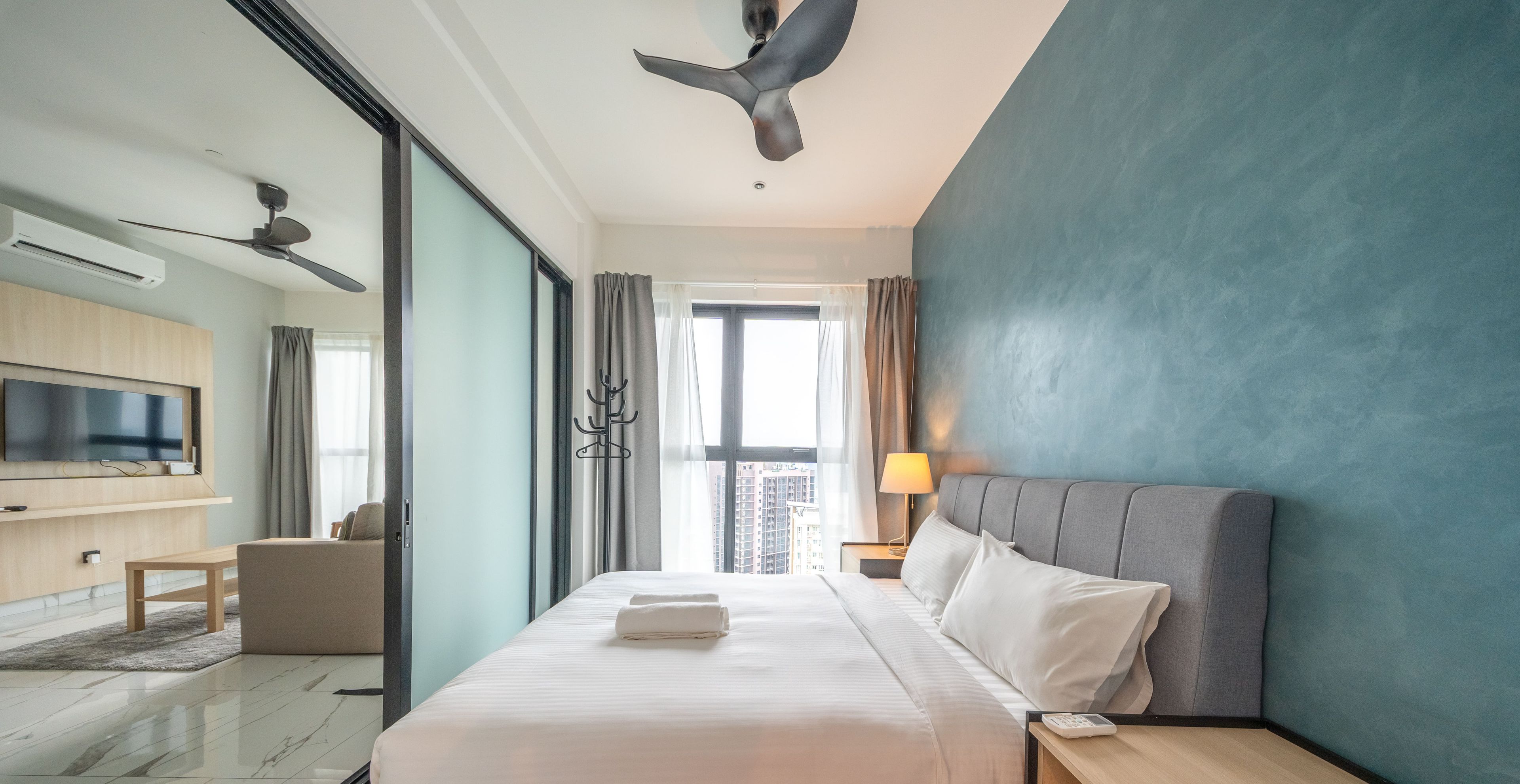 Una habitación de hotel moderna con una cama grande, un televisor de pantalla plana, un ventilador de techo y vistas a la ciudad.