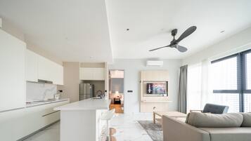 Una cocina moderna con armarios blancos, una isla central con taburetes de bar, un ventilador de techo y un amplio ventanal que proporciona luz natural.