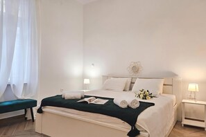Una habitación de hotel con cama, una mesita de noche con lámpara, un banco y una ventana con cortinas.