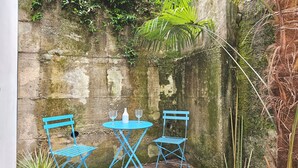 A small outdoor seating area with two blue metal chairs and a matching table, set against a moss-covered stone wall.