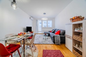 Una sala de estar moderna con comedor, un sofá gris, una silla roja, una mesa de centro de vidrio y una alfombra roja.