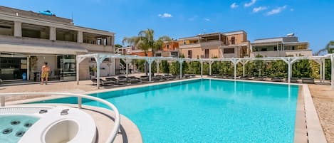 A swimming pool with a hot tub, lounge chairs, and a covered seating area.