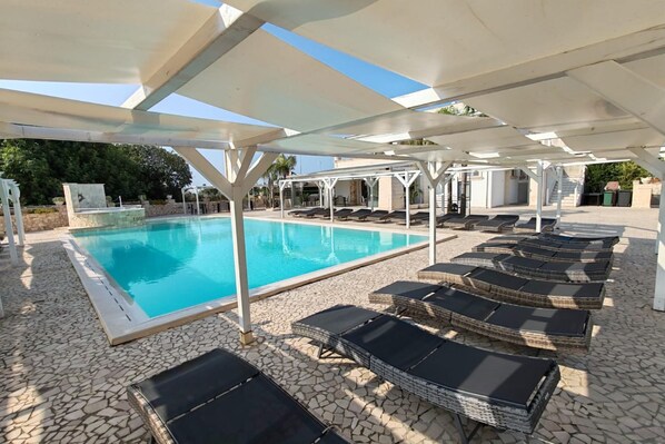 A pool area with lounge chairs and a covered seating area.