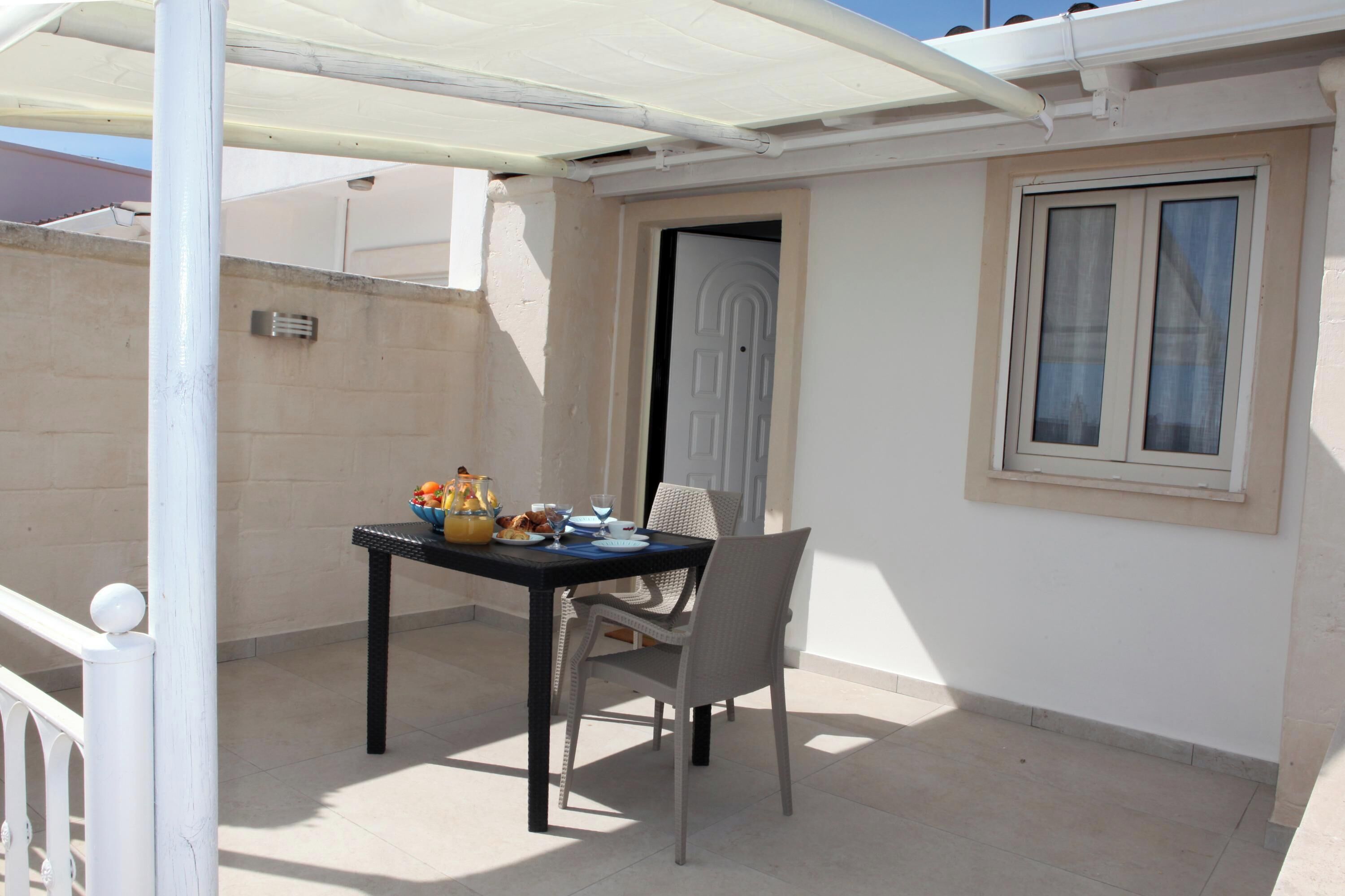 Eine Terrasse mit Tisch für zwei Personen, einem Stuhl und einem Fenster mit Blick auf die Straße.