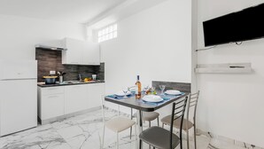 Cocina compacta con armarios blancos, horno empotrado, piso de baldosas de mármol y un comedor con una mesa preparada para dos personas.