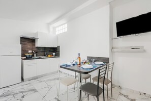 Una cucina compatta con mobili bianchi, forno integrato, pavimento in marmo e zona pranzo con tavolo apparecchiato per due.