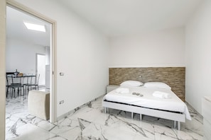 Una habitación de hotel pequeña y moderna con una cama, cabecera de madera y piso de baldosas de mármol.