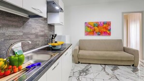 A modern kitchen with a built-in stove, a sink, and a countertop. There is a beige sofa and a colorful abstract painting on the wall. - Pino 6 - 2 bedrooms Near The Sea, Nardò, Italy (Nardò)