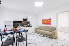 Una cocina moderna con armarios blancos, una mesa de comedor con sillas y un sofá en la sala.