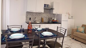 Un coin repas avec une table dressée pour quatre personnes, des chaises, une cuisine en arrière-plan et un canapé avec un coussin.