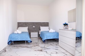 Une chambre d’hôtel avec deux lits, un sol en marbre, une commode et un miroir.