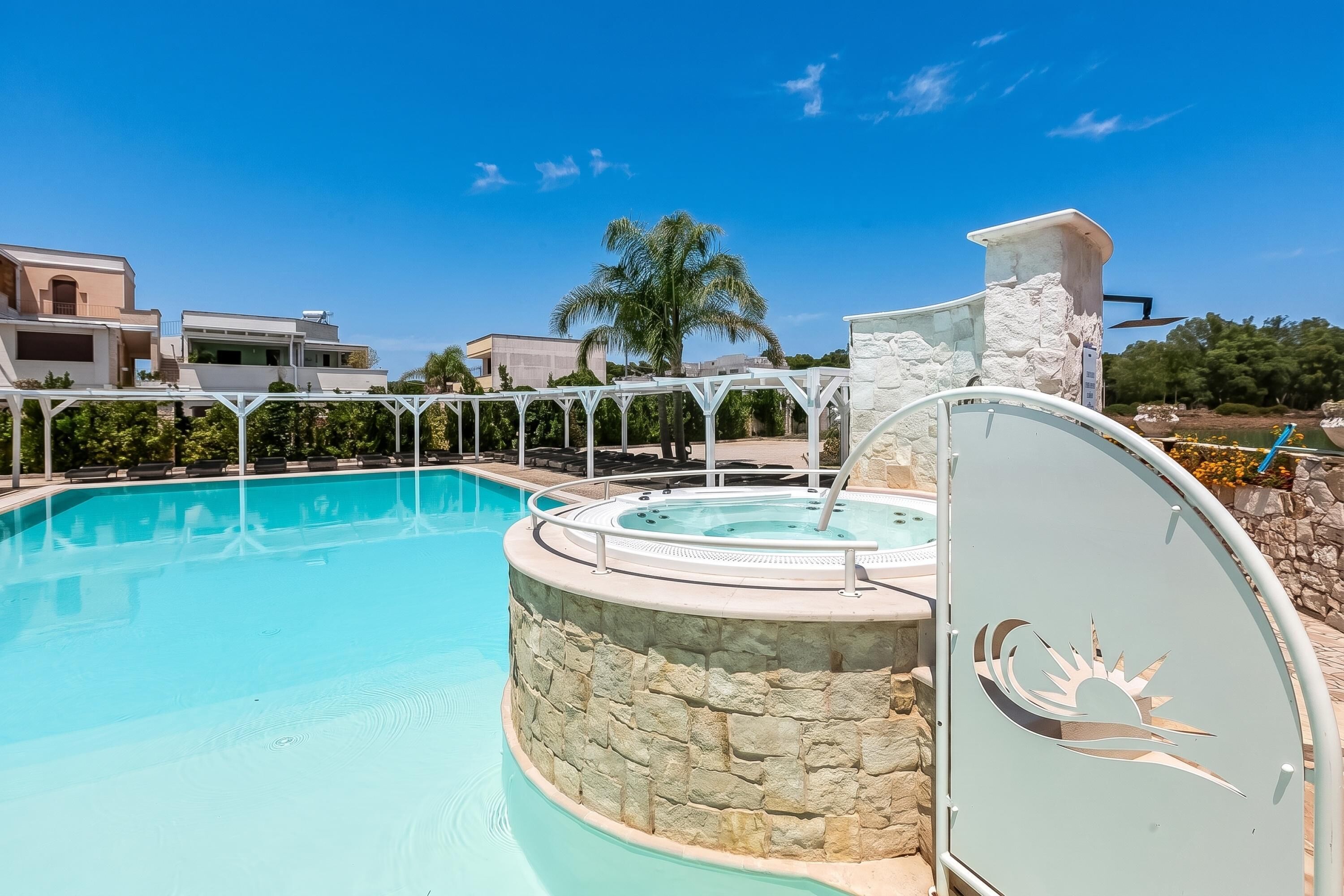 A swimming pool with a stone wall, a hot tub, and a covered seating area.