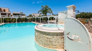 Una piscina con parete in pietra, vasca idromassaggio e area relax coperta.