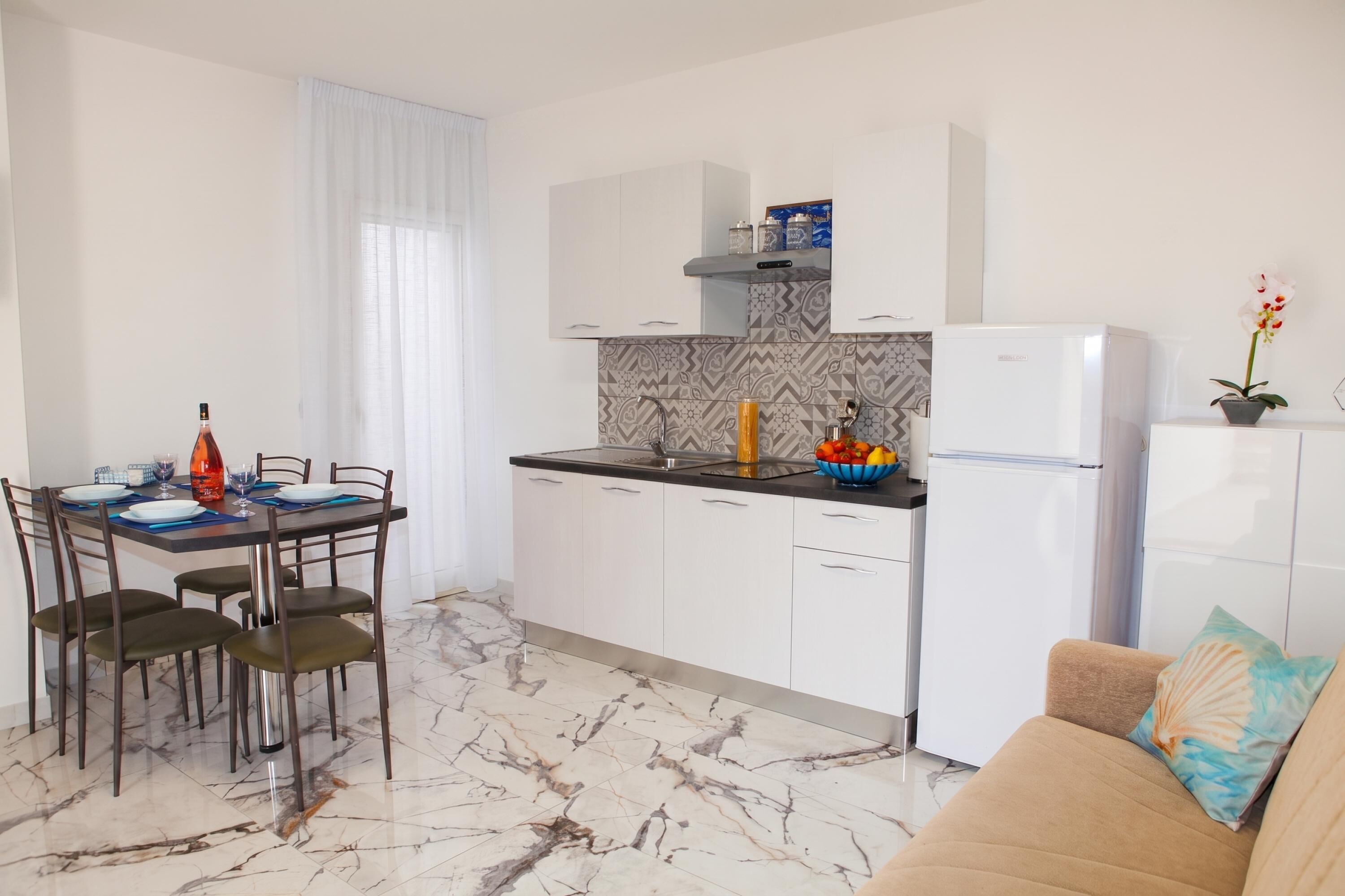 Una cucina moderna con mobili bianchi, un pavimento in marmo e un'area pranzo con un tavolo apparecchiato per due.