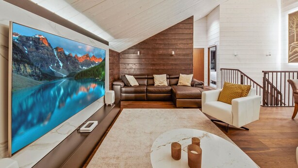 A modern living room with a large flat-screen TV, leather sofas, a white armchair, and a marble coffee table.
