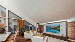 A modern living room with a large TV, comfortable seating, a fireplace, and a view of a mountain landscape.