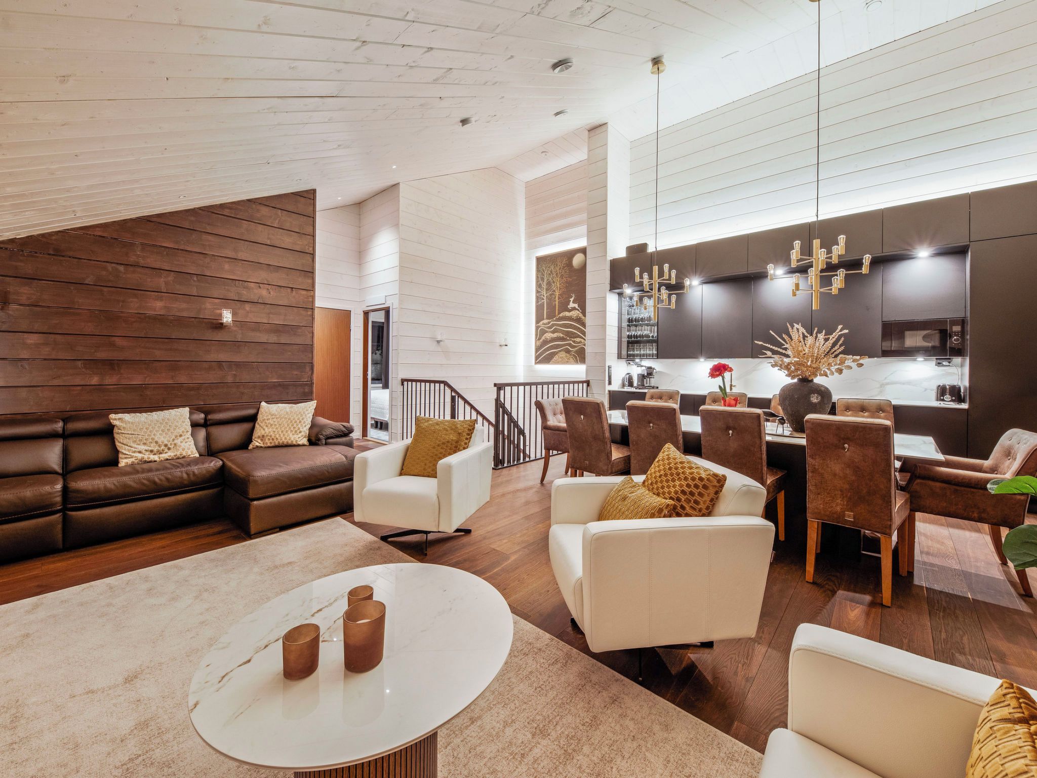 A modern living room with a brown leather sofa, white armchairs, and a marble coffee table.