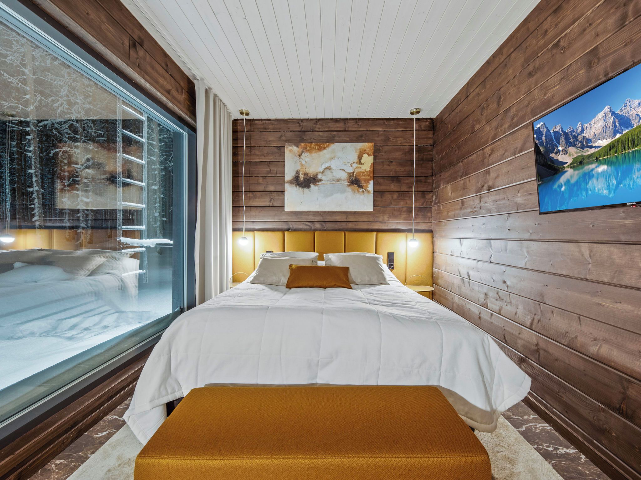 A modern bedroom with a large window, a bed with white bedding, a wooden headboard, and a painting on the wall.