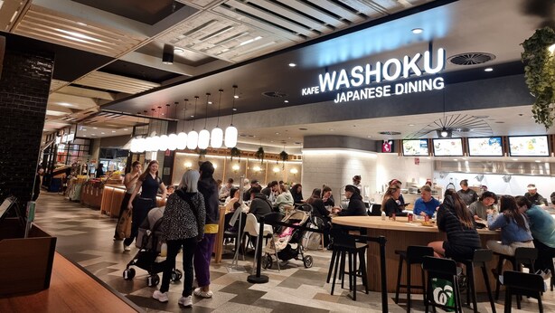 Un restaurant japonais proposant une cuisine raffinée, doté d’un intérieur moderne, notamment d’un plafond haut avec des poutres apparentes et des luminaires suspendus.