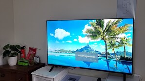 Un téléviseur à écran plat posé sur une commode blanche dotée de tiroirs, qui diffuse une image d’une plage tropicale.