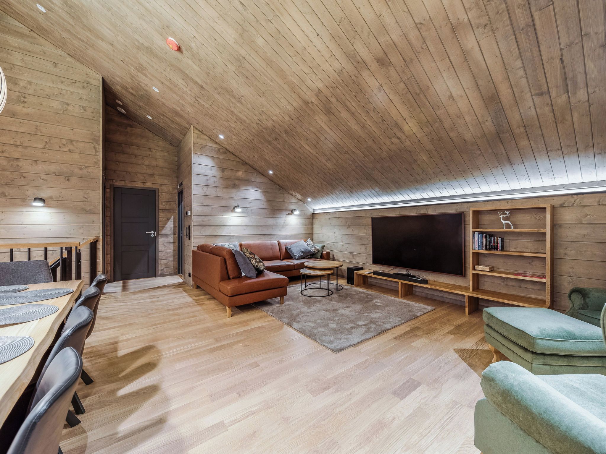 Una sala de estar moderna con techo de madera, un televisor de pantalla plana grande, un sofá, una mesa de centro y una estantería.