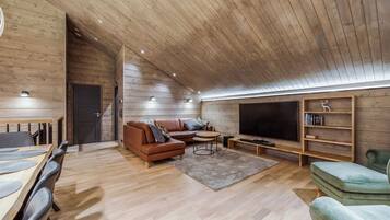 A modern living room with a wooden ceiling, a large flat-screen TV, a sofa, a coffee table, and a bookshelf.