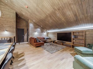 Een moderne woonkamer met een houten plafond, een grote flatscreen televisie, een bank, een salontafel en een boekenplank.