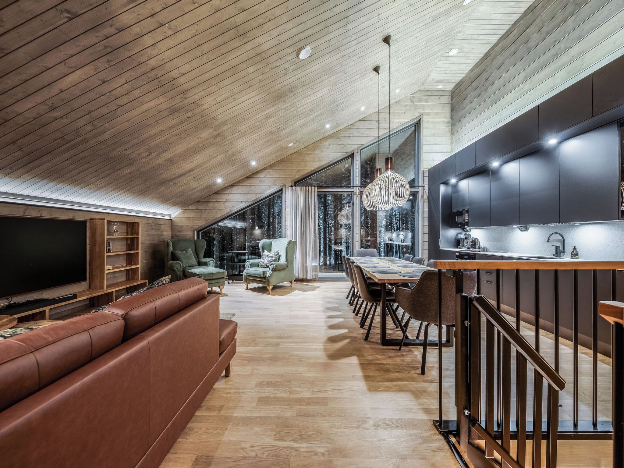 Un interior moderno con techo de madera, comedor, cocina con una isla grande y zona de estar con sofá y televisor.