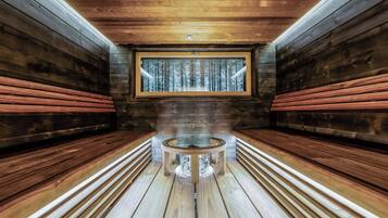 A sauna room with wooden benches, a central table, and a window with a snowy forest view.