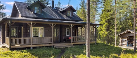 A log cabin with a porch, a chimney, and a small adjacent structure.
