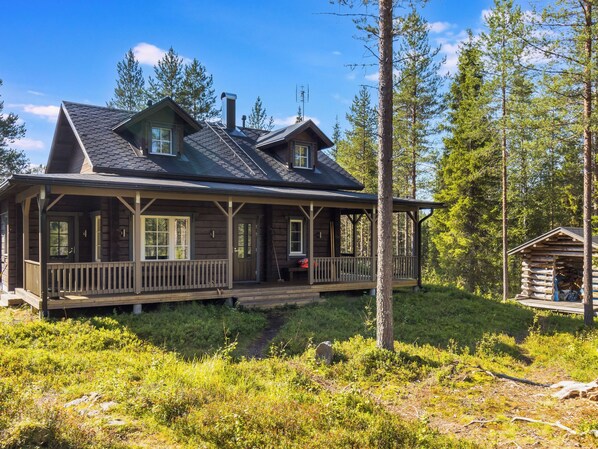 A log cabin with a porch, a chimney, and a small adjacent structure.