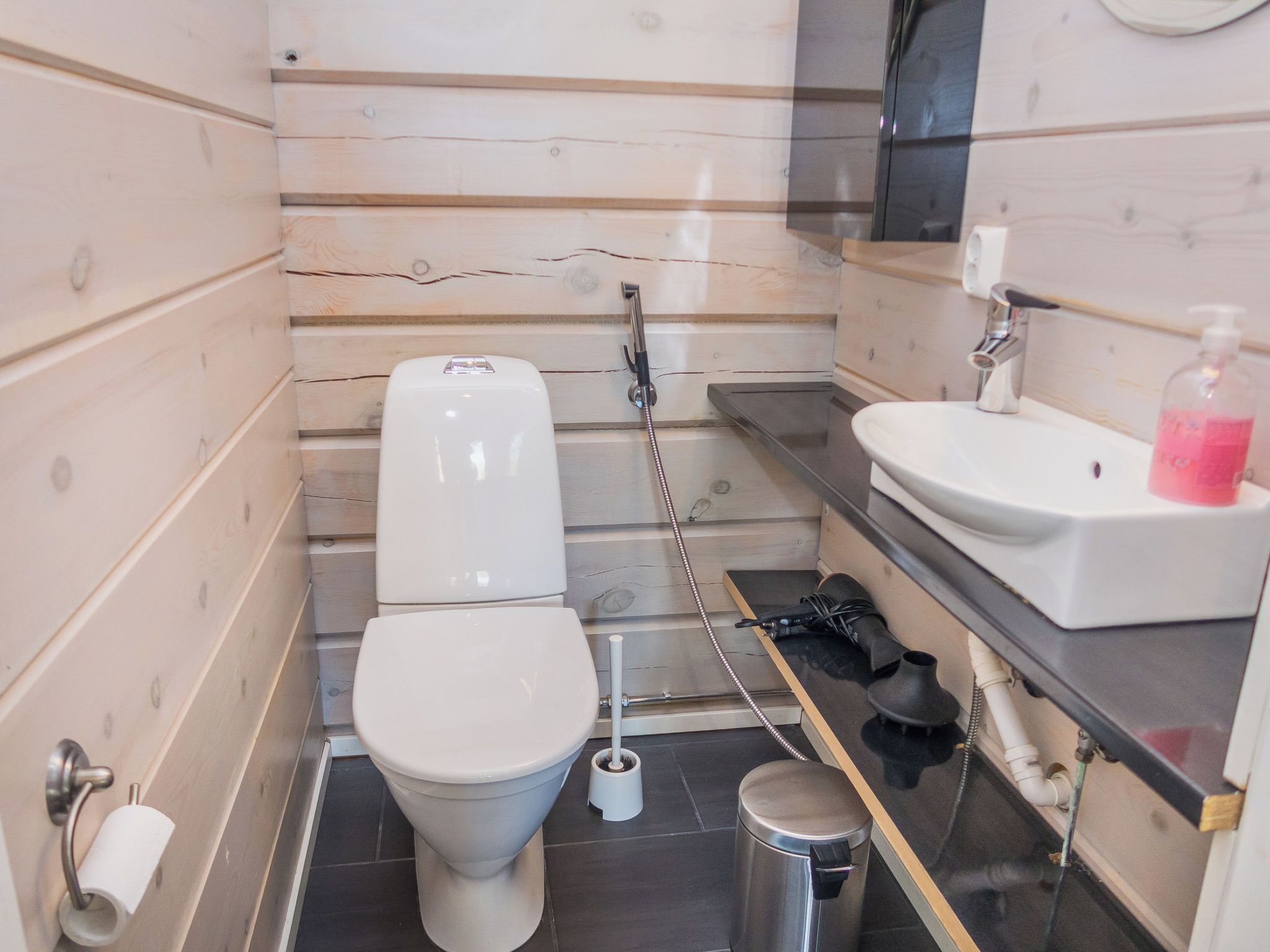 A compact bathroom with a toilet, a bidet, a sink, and a trash bin.