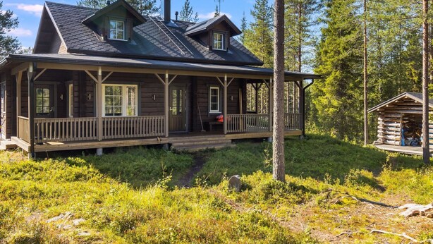 Une cabane en rondins dotée d’une véranda, d’une cheminée et d’une petite construction adjacente.