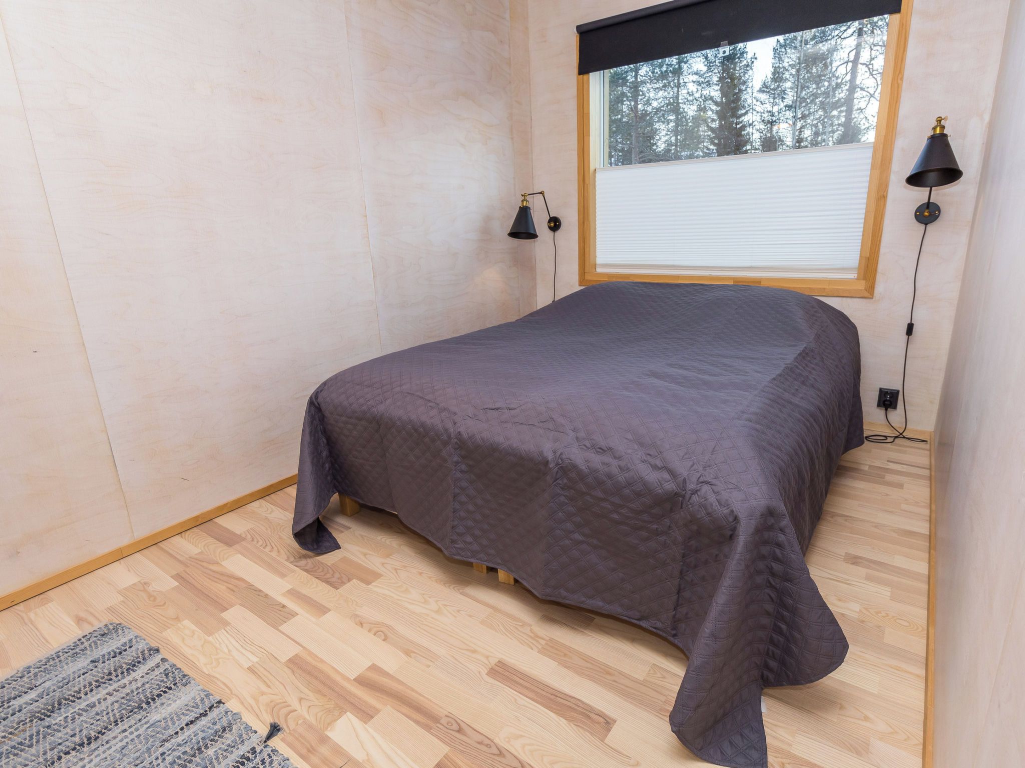 Ein Schlafzimmer mit einem Bett, einem Fenster mit Jalousien, einer Lampe und einem Teppich.