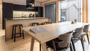 A modern kitchen with a central island, a dining area with a long table and chairs, and large windows with blinds. - Villa plywood by Interhome (Pudasjärvi)