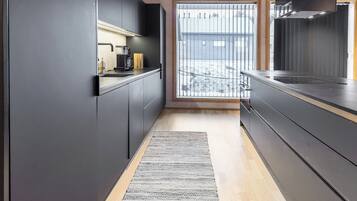 A modern kitchen with dark cabinetry, a coffee machine, and a view through a window to a snowy outdoor area.