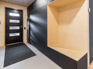 Ein Flur mit einer schwarzen Tür, einem Kühlschrank und einem Holzregal.
