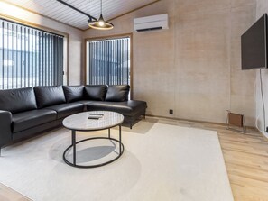 Ein modernes Wohnzimmer mit einem Ecksofa, einem runden Couchtisch und einem großen Fenster mit Jalousien.